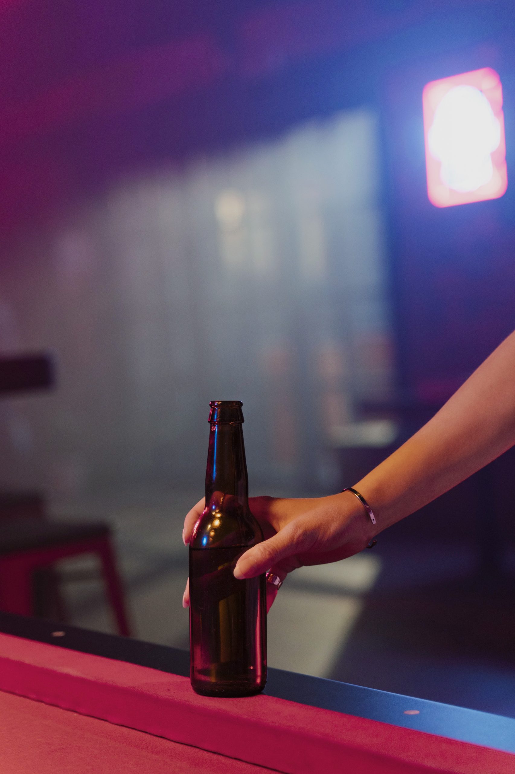 Person holding a beer bottle as it sits on the edge of a pool table. Drinking? Never drive.