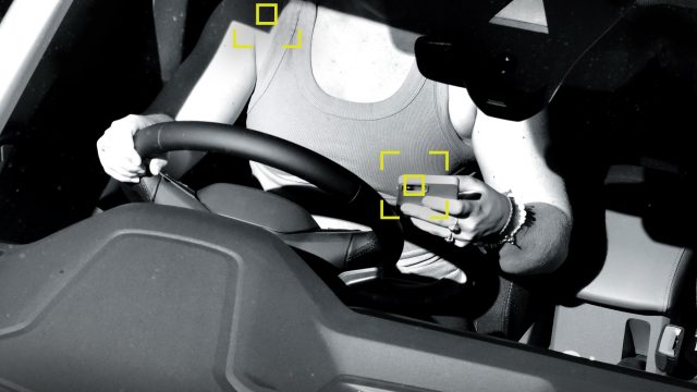 Image captured on seatbelt and mobile phone camera of a woman using her phone while driving