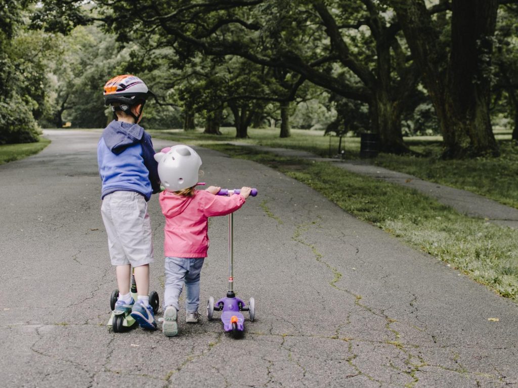 Two young children riding scooters on a paved path