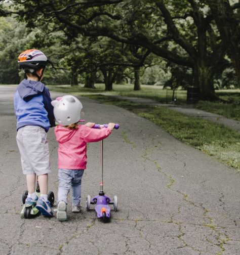 Two young children riding scooters on a paved path