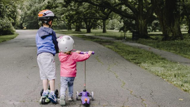Two young children riding scooters on a paved path