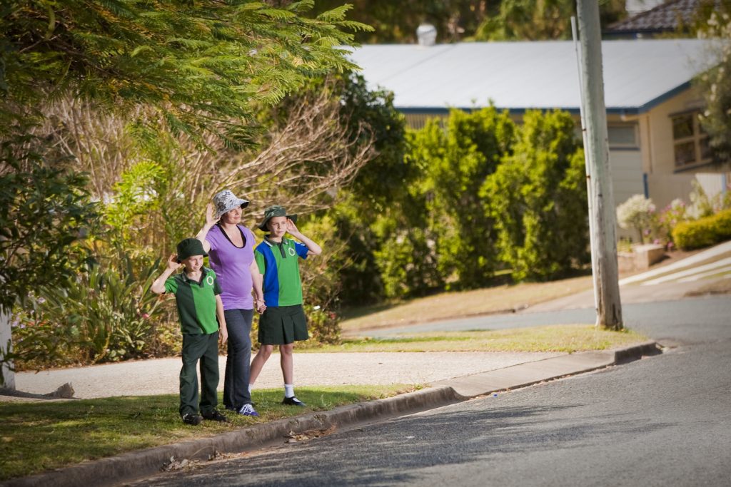 Two school children and their mother prepare to cross the road