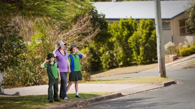 Two school children and their mother prepare to cross the road