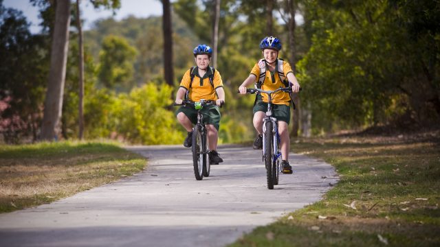 Two school children riding bikes on a footpath