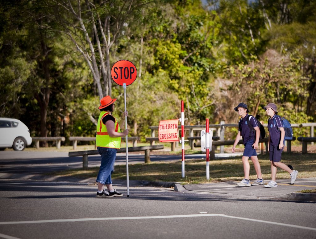 Two children wait before the crossing in front of traffic controller with the stop sign