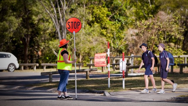 Two children wait before the crossing in front of traffic controller with the stop sign