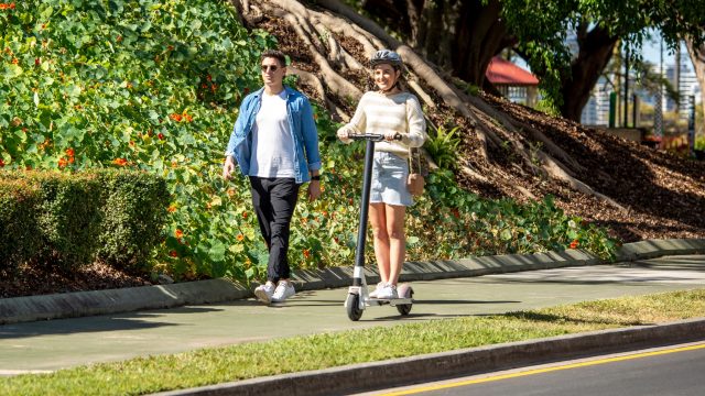 Person riding an e-scooter on footpath next to walking pedestrian