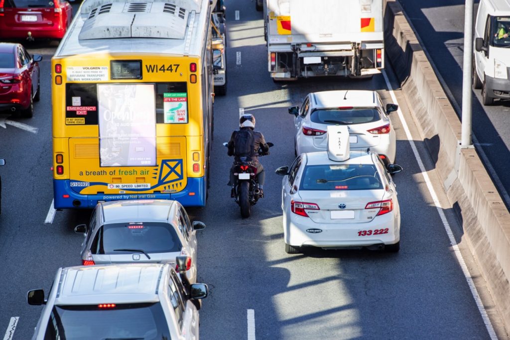 Stopped traffic on a road with a bus, cars, taxi and motorbike rider