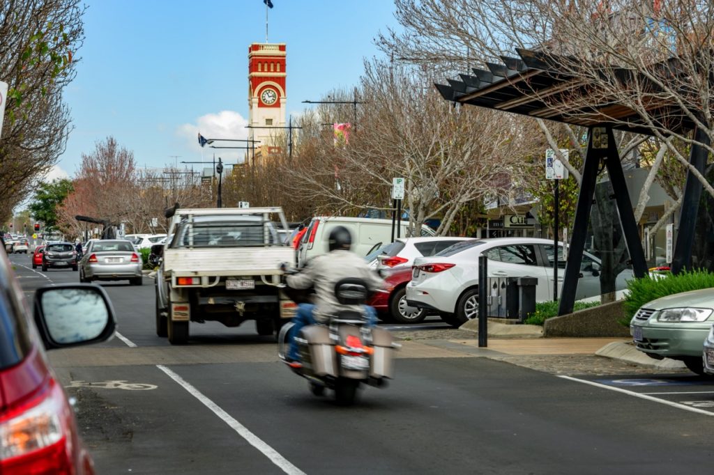 Motorcycle and car travel down busy Toowoomba street.