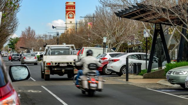 Motorcycle and car travel down busy Toowoomba street.