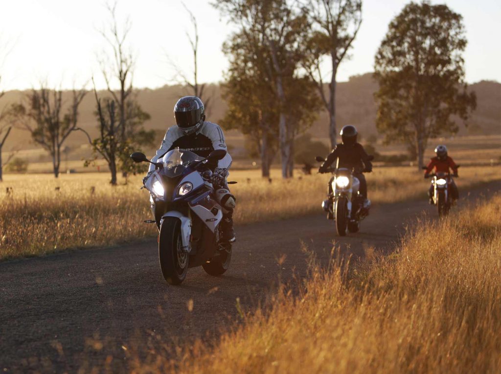 Three motorcycle riders going through a rural road at sunset